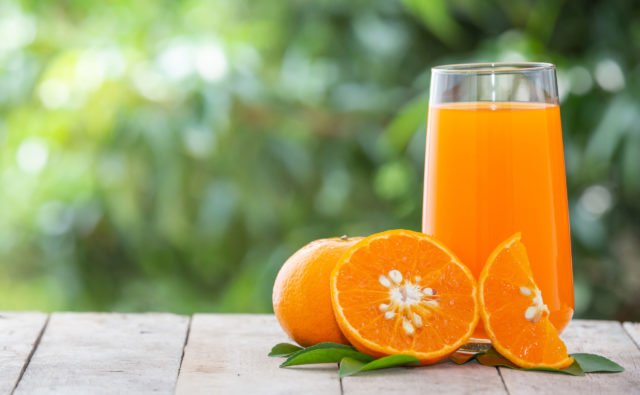 The orange juice is in a glass and the orange fruit is placed beside it with a green natural background.